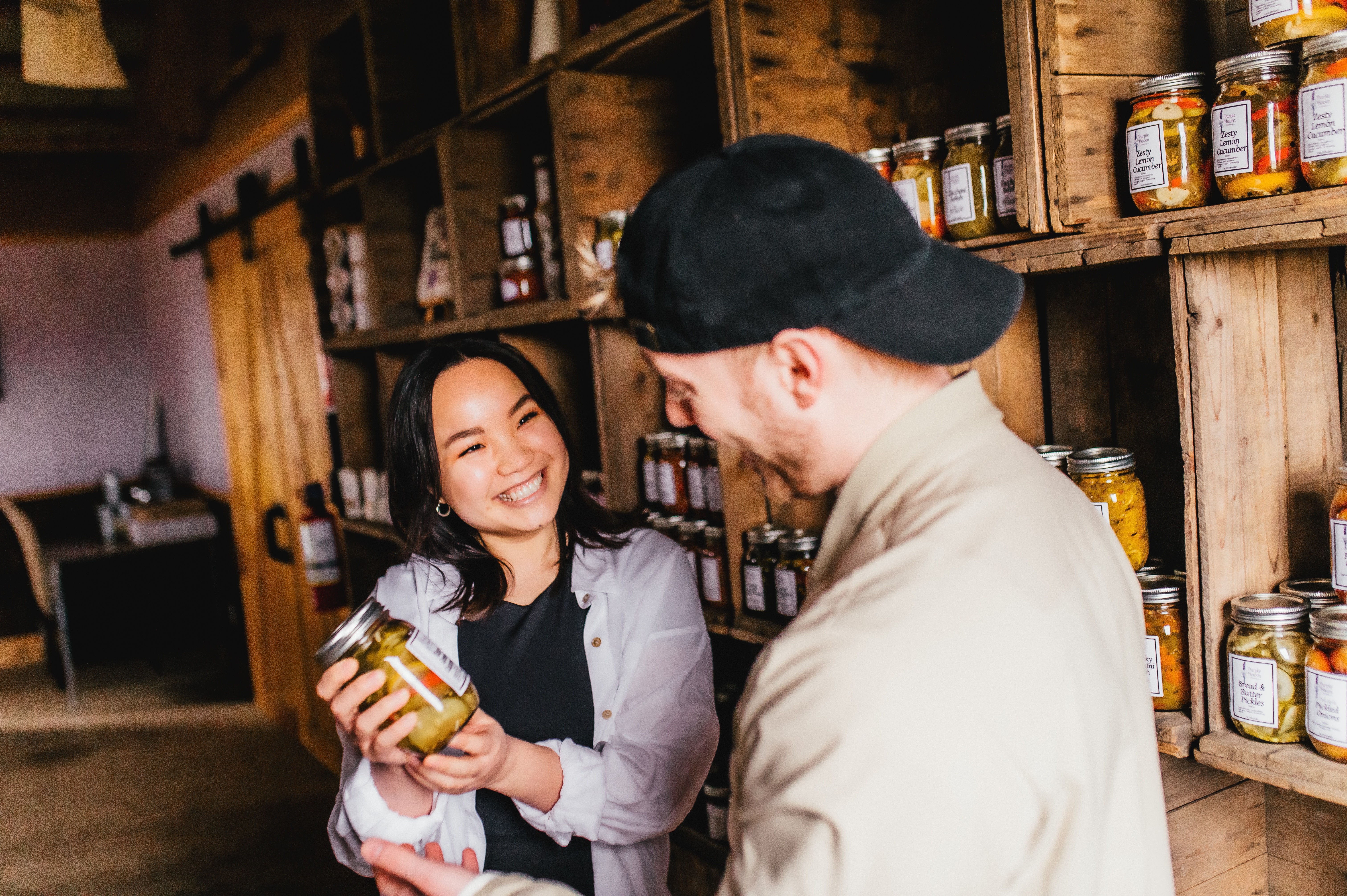 A woman and man smile over a jar of pickles