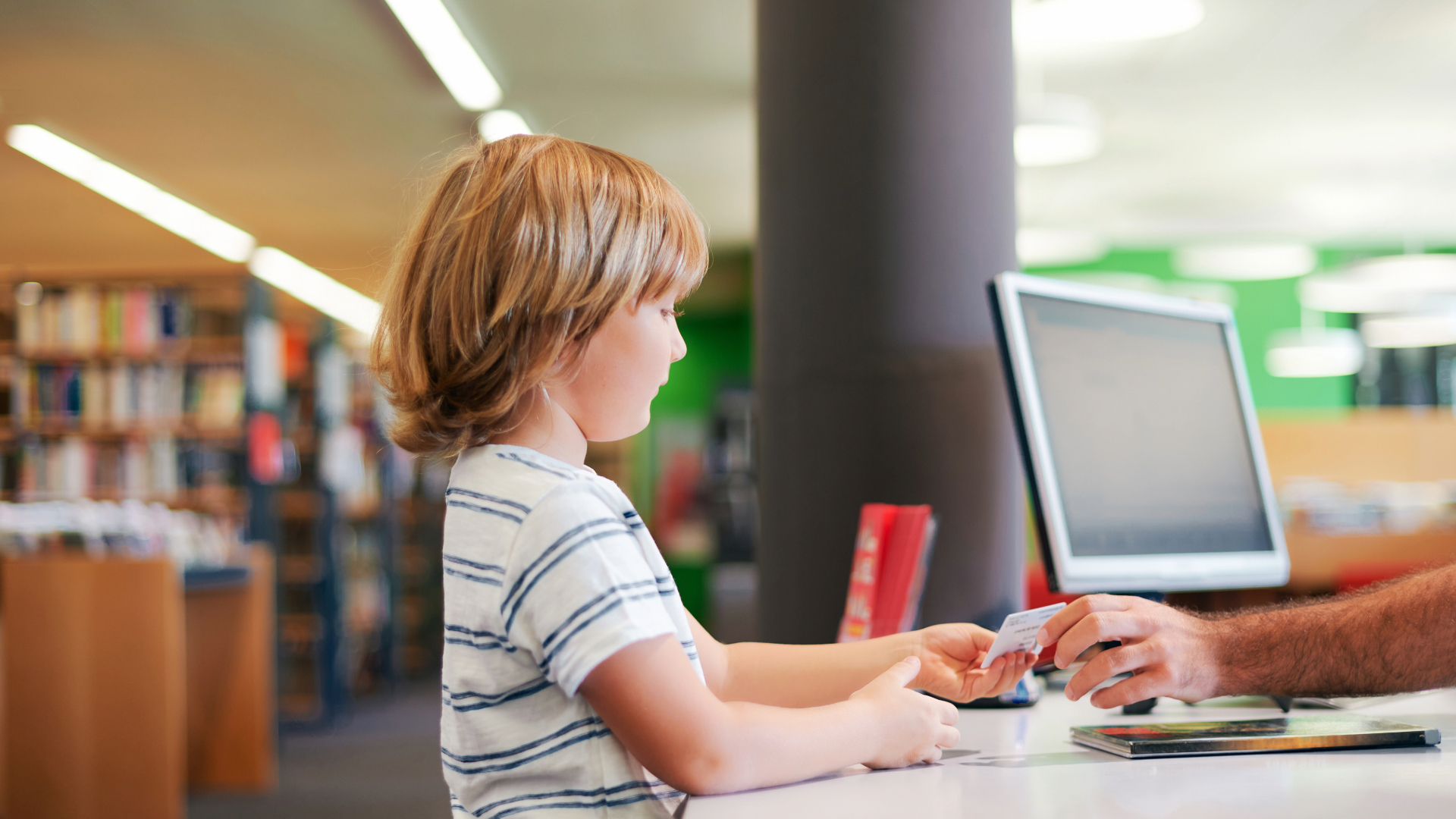 Little boy checking out a book with library card