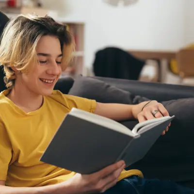 Teen boy reading a book on the couch